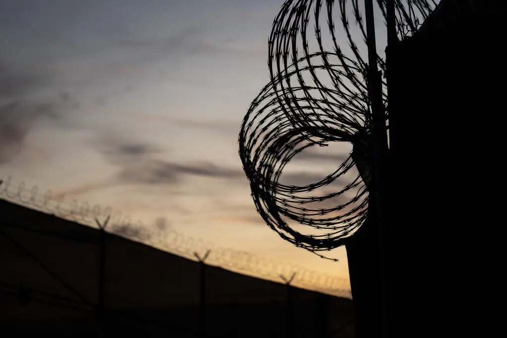 Fences topped with razor wire set against a dimly lit sky.