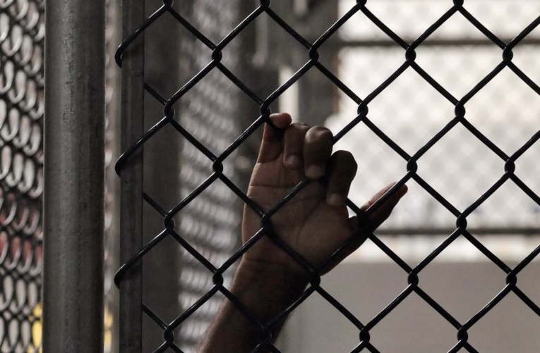 The hand of a Guantanamo detainee is seen holding onto a fence