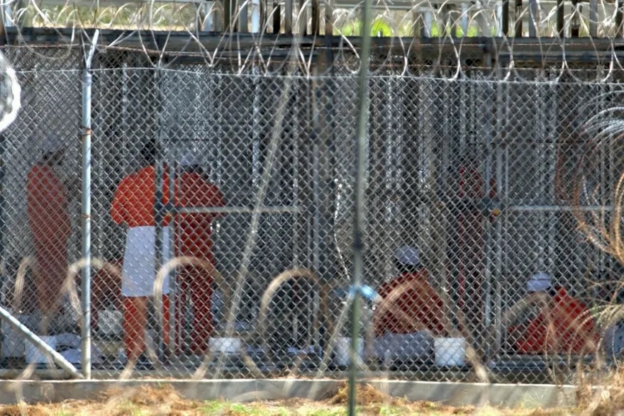 Detainees behind a fence in orange jumpsuits