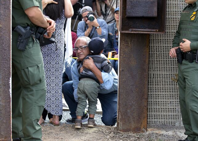 Una familia mexicana se abraza en la frontera mientras dos agentes fronterizos observan / Earnie Grafton