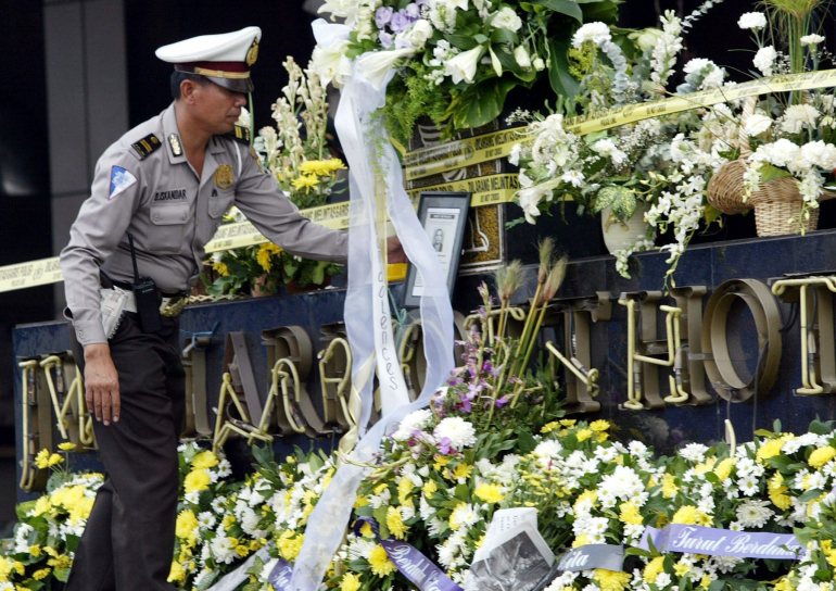 Un oficial de polica indonesio mira los ramos de flores blancas que quedaron en el letrero destrozado del hotel JW Marriott de Yakarta mientras se oraba por los muertos en el atentado de agosto de 2003.