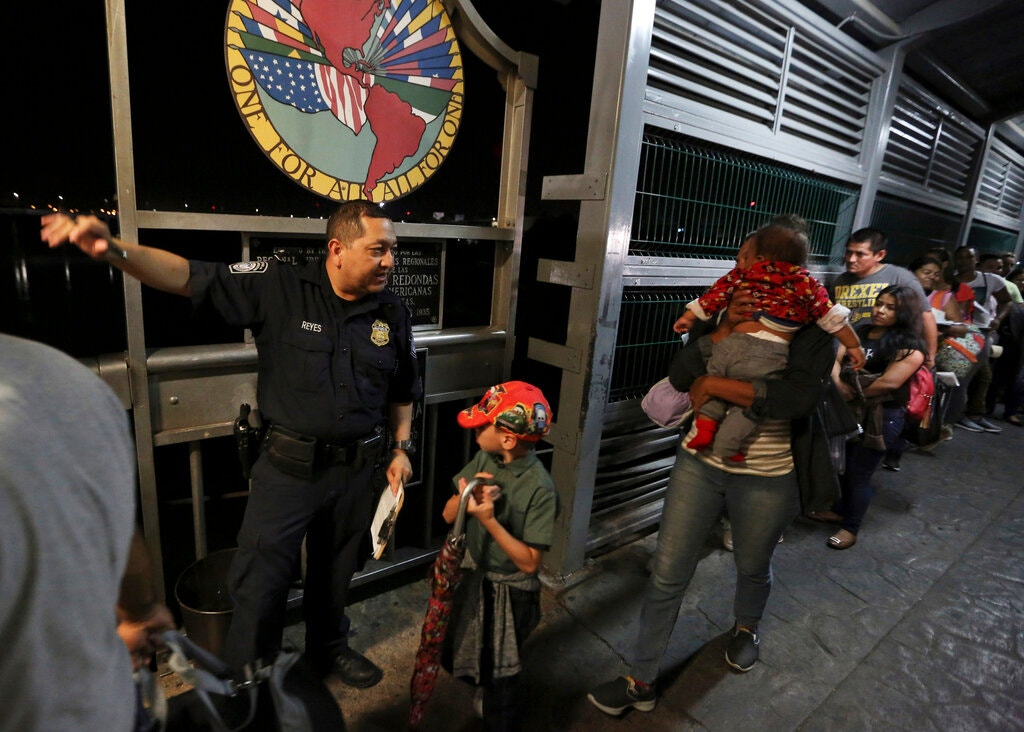 Un oficial de la Oficina de Aduanas y Protección Fronteriza de Estados Unidos guía a los solicitantes de asilo a través del puente internacional desde Nuevo Laredo, México, hacia Estados Unidos.